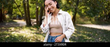 Das stilvolle asiatische Mädchen geht im Park spazieren, lacht und genießt das Sommerwetter. Menschen- und Lifestyle-Konzept Stockfoto