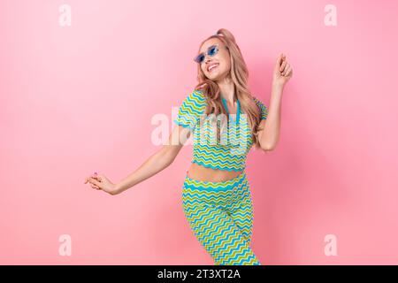 Porträt des fröhlichen hübschen Mädchens mit Schwänzen Friseur gekleidet bunter Anzug in blauer Sonnenbrille Tanz haben Spaß isoliert auf rosa Farbe Hintergrund Stockfoto