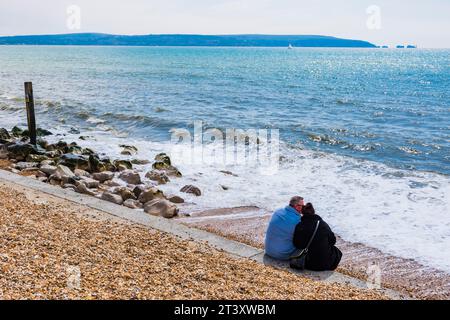 Ein Paar sitzt am Meer, die Needles und der Rest der nordwestlichen Isle of Wight im Hintergrund. Milford on Sea, New Forest, Hampshire, Engl Stockfoto