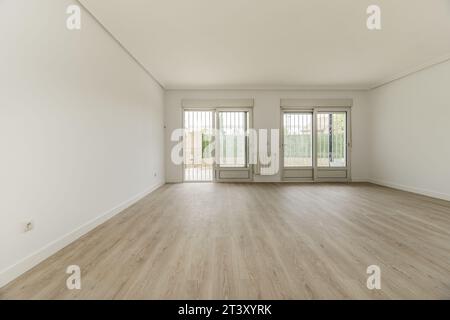 Wohnzimmer eines leeren Hauses mit weiß lackierten Wänden, großen Schiebetüren aus Aluminium und weißem Glas, Sicherheitstüren und Holzböden Stockfoto