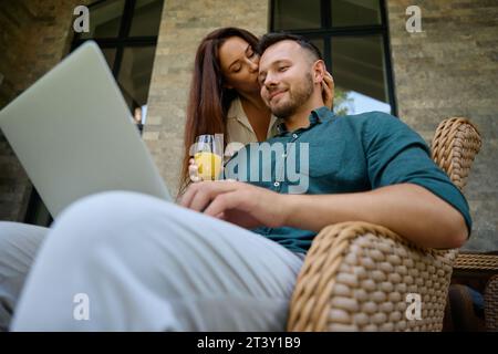 Der Mann sitzt in einem Korbstuhl und arbeitet am Laptop Stockfoto