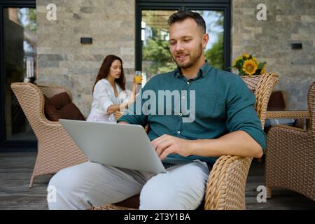 Der Mann sitzt im Korbstuhl und arbeitet am Laptop Stockfoto