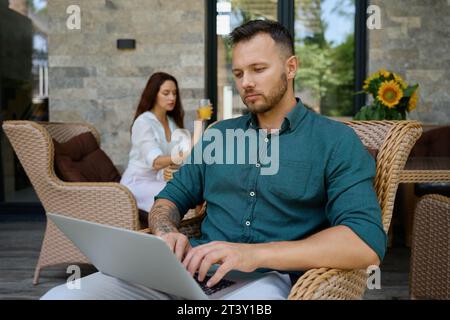 Der Mann sitzt in einem Korbstuhl und arbeitet am Laptop Stockfoto