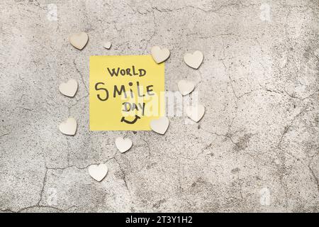 World Smile Day Schreiben Sie in eine Papiernote und weiße Herzen auf einem grauen Steinhintergrund in einer Draufsicht Stockfoto