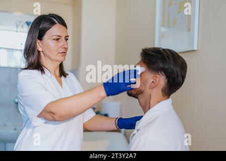 In einem Krankenhausuntersuchungsraum kontrolliert ein Arzt den Blutdruck, testet den Blutzucker, untersucht die Ohren und bietet professionelle medizinische Betreuung. Stockfoto