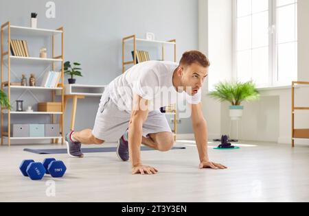 Schöner, sportlicher junger Mann in weißem T-Shirt, der zu Hause auf dem Boden sportliche Übungen macht. Stockfoto