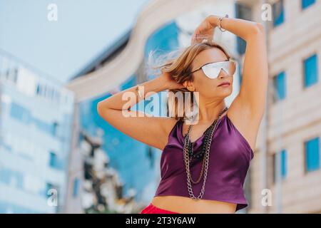 Selbstbewusste Frau in trendiger Urban Fashion posiert anmutig vor einer wunderschönen modernen Stadtkulisse Stockfoto