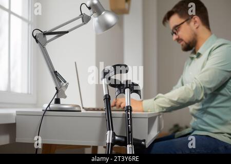 Crutchers nähern sich dem Hintergrund eines Mannes, der im Büro an einem Laptop arbeitet. Stockfoto
