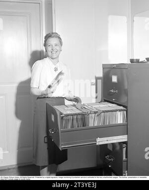 Frau im Amt in den 1940ern Eine junge Frau in einer weißen Bluse und Rock, die in einem Aktenschrank arbeitet, wo sie die Dokumente in die richtigen Ordner sortiert. Schweden 1949. Kristoffersson Ref. AR49-3 Stockfoto