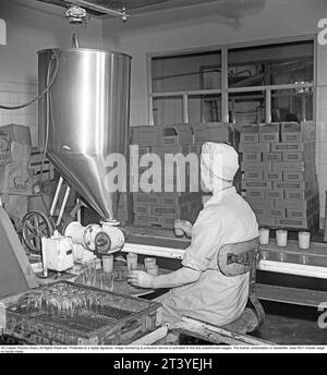 Arbeitsplätze in den 1940er Jahren Innenausstattung aus den Fabriken des Lebensmittelunternehmens Winborg, wo eine weibliche Mitarbeiterin an einer Maschine sitzt, die Glasgläser füllt, die sie dann auf ein Förderband stellt, damit der Becher zum nächsten Arbeiter kommt, der einen Deckel aufschraubt. Schweden 1949. Kristoffersson Ref. AM2-4 Stockfoto