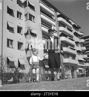 Einen Tag im Mai 1940. Eine Mutter hält ihren Sohn in der Hand, während sie auf einer Straße in Stockholm spaziert. Im Hintergrund ein Wohnhaus und Wohnungen. Sie ist in typischer 40er-Mode gekleidet. Ein Kleid mit Kreidestreifen, passendem Rock, Jacke und wunderschöner Hut. Schweden Stockholm Mai 1940. Kristoffersson Ref. 133-21 Stockfoto