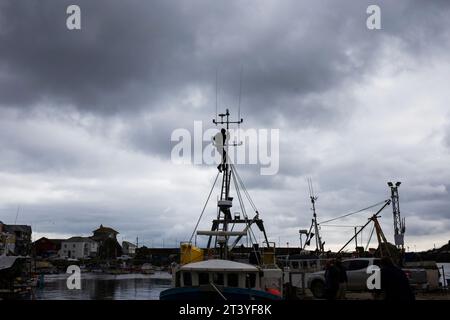 Mevagissey in Cornwall-Serie - Silhouette eines Mannes auf dem Bootsmast vor einem graubewölkten Himmel im Hafen Stockfoto