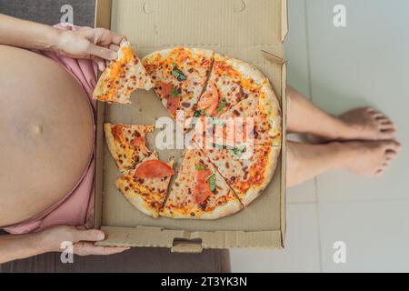 Eine schwangere Frau genießt ein Stück Pizza und genießt einen Moment der Genussfreude, während sie ihr Verlangen nach einer köstlichen, wohltuenden Leckerei befriedigt. Begeistert Stockfoto