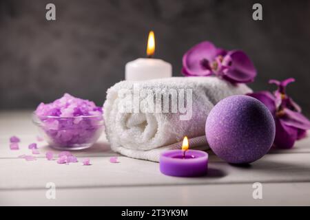 Lila Badebombe, Meersalzkristalle, Handtuch und Duftkerzen auf Holztisch. Körperhautpflege. Wellness-Spa Stockfoto