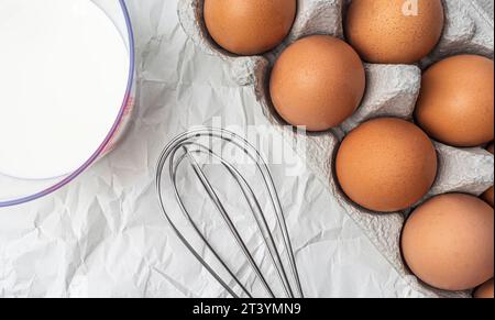 Milch, Eier in einer Kiste und Schneebesen zum Schlafen auf weißem Hintergrund von oben Stockfoto