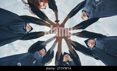 Team von College- oder Universitätsstudenten, die den Abschluss feiern. Gruppe glücklicher erfolgreicher Absolventen in akademischen Hüten und Gewändern, die im Kreis stehen und Stockfoto