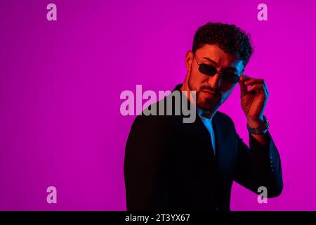 Studio-Aufnahme des hübschen, lächelnden jungen Mannes in stilvoller Sonnenbrille isoliert auf rosa Farbverlauf Hintergrund im Neonlicht. Copyspace für Werbung Stockfoto