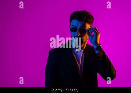 Studio-Aufnahme des hübschen, lächelnden jungen Mannes in stilvoller Sonnenbrille isoliert auf rosa Farbverlauf Hintergrund im Neonlicht. Copyspace für Werbung Stockfoto