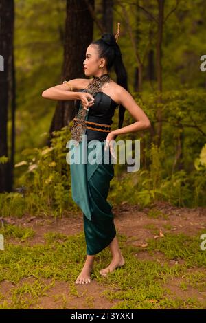 Wunderschöne indonesische Tänzer mit traditionellen grünen Kostümen und schwarzen Haaren, die nach der Aufführung im Wald posieren Stockfoto