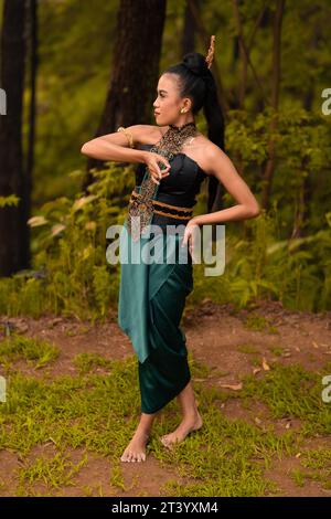 Wunderschöne indonesische Tänzer mit traditionellen grünen Kostümen und schwarzen Haaren, die nach der Aufführung im Wald posieren Stockfoto