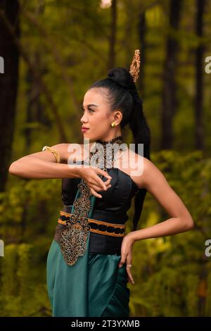 Wunderschöne indonesische Tänzer mit traditionellen grünen Kostümen und schwarzen Haaren, die nach der Aufführung im Wald posieren Stockfoto