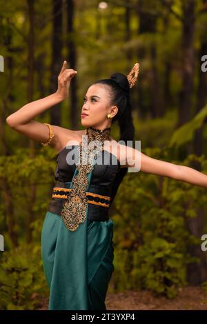 Wunderschöne indonesische Tänzer mit traditionellen grünen Kostümen und schwarzen Haaren, die nach der Aufführung im Wald posieren Stockfoto