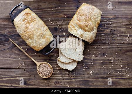 Über dem Tisch sehen Sie frisch gebackene Vollkornbrotlaibe mit Holzlöffel gefüllt mit Getreide. Gemeinkosten. Stockfoto