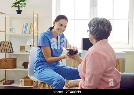 Freundliche Krankenschwester gibt älteren Frauen kleine Massagekugeln, um die Triggerpunkte am Körper zu massieren. Stockfoto