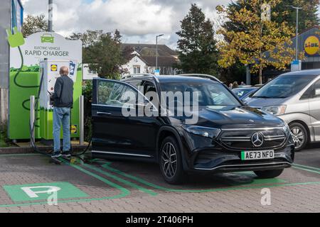 Mann, der seine Autobatterie an einem Schnellladegerät eines Elektrofahrzeugs in einem Lidl-Supermarkt in England auflädt Stockfoto