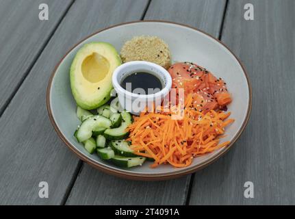 Salmon Poke Schüssel mit Cut an Avocado, Gurke, Karotten und Quinoa Sprinkle mit Sesamsamen serviert mit Sojasauce auf Keramikschale. Organisch und heilt Stockfoto