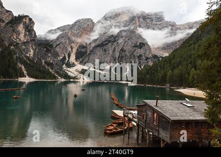 Bootshaus am Pragser See mit dem majestätischen Gipfel der Croda del Becco (Seekofel) in den Wolken. Holzboote auf dem See. Stockfoto