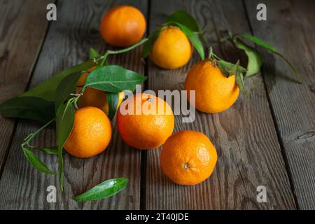 Mandarinen (Orangen, Clementinen, Zitrusfrüchte) mit Blättern auf hölzernem Hintergrund. Mandarinorangen mit Blättern. Stockfoto