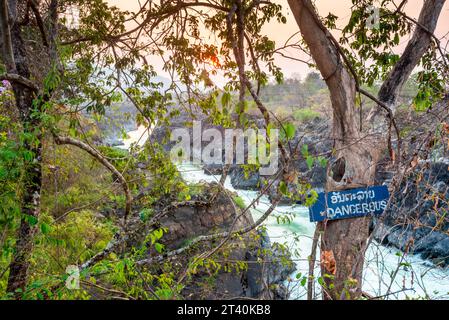 Blick von felsigen Klippen, bei Sonnenuntergang. Sonnenlicht scheint auf Felsen, neben verschwommenem Wasser, das vorbeirauscht, an den wichtigsten Wasserfällen und Stromschnellen von Don Khon Stockfoto