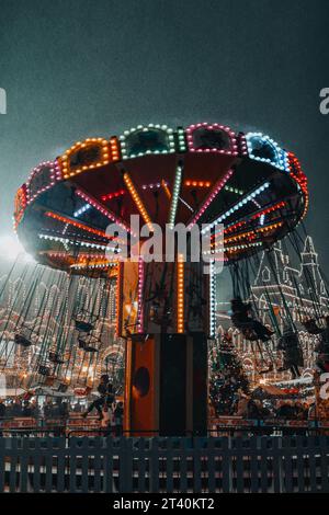 Winter in der Nacht. Glühendes festliches Karussell, das auf der Straße unter dem fliegenden Schnee wirbelt. Stockfoto