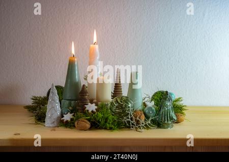 2. Adventsdekoration mit vier verschiedenen Kerzen, zwei sind beleuchtet, grüne Glas-Weihnachtskugeln, Moos- und Zimtsterne auf einem Holztisch gegen ein l Stockfoto