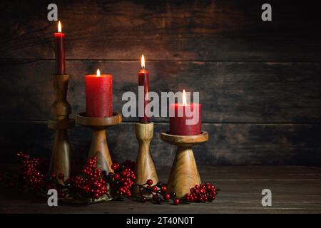 Vier rote Kerzen in hölzernen Kerzenstäben hintereinander als Adventsdekoration oder Weihnachtsdekoration vor einem dunklen rustikalen Hintergrund, natürliche Ferienwohnkultur, Kopie Stockfoto