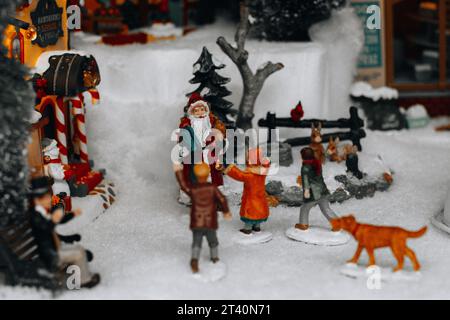 Weihnachtsfiguren von Weihnachtsmann und Kindern, die in der verschneiten Straße spielen. Weihnachtsgeschenke und -Dekorationen. Stockfoto