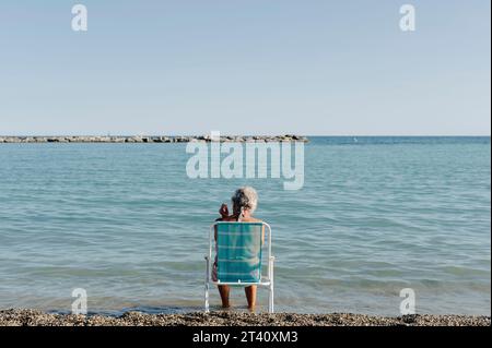 Eine ältere Frau sitzt am Meer, um ihre körperliche Gesundheit dank Jod und Sonnenstrahlen zu verbessern Stockfoto