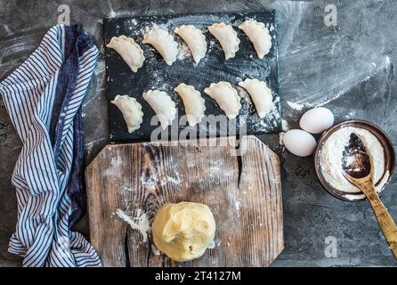 Blick von oben auf Teig und Varenyky. Mehleier, Himbeeren und Pin auf rustikalem Holzbrett, dunkler Hintergrund Stockfoto