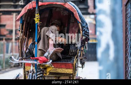 Kathmandu, Nepal - 06. Oktober 2017: Rikscha-Fahrer mittleren Alters sitzt mit überkreuzten Beinen in der Kabine seiner Rikscha und wartet auf Kunden. Stockfoto