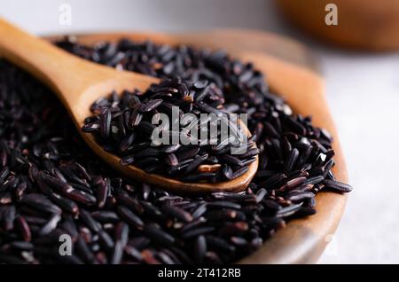 Nahaufnahme von rohem schwarzem Reis in einer Tonschale mit einem Holzlöffel. Stockfoto