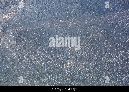 Gebrochenes gehärtetes Glas in Rissen, verdorbene Glasoberflächentextur auf blauem Himmel Hintergrund, Glanz von hellem Licht, Nahaufnahme. Stockfoto