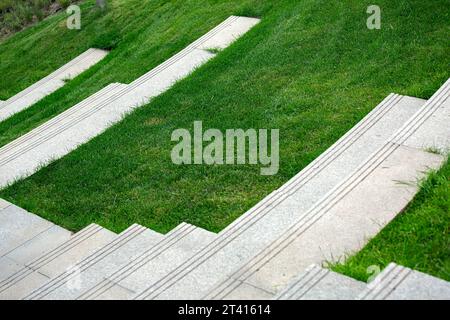 Treppen mit Granitstufen in der Nähe des Rasenplatzes auf dem Hügel im Sommerpark, niemand. Stockfoto