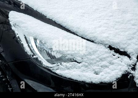Halogenscheinwerfer vorne eines schwarzen Autos, bedeckt mit einer Schneeschicht an einem kalten Wintertag, Nahaufnahme Fahrzeugbeleuchtung unter einer Schneelage, niemand. Stockfoto