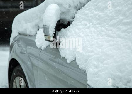 Seitlicher Rückspiegel mit schneebedecktem Blinker an einem verschneiten Wintertag, Nahaufnahme eines von Niederschlag bedeckten Fahrzeugs. Stockfoto
