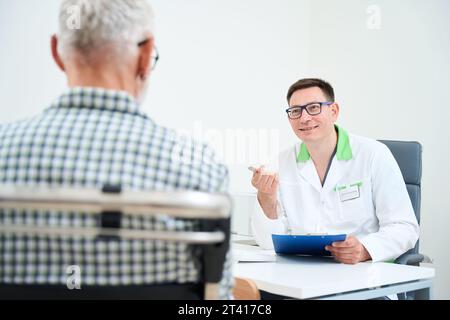 Ein Mann in einem medizinischen Kleid kommuniziert mit einem alten Mann Stockfoto