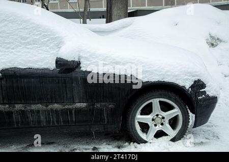 Schmutziges schwarzes Auto, Seitenansicht, mit schneebedeckten Passagiertransporten an einem kalten Wintertag auf einer Stadtstraße, niemand. Stockfoto