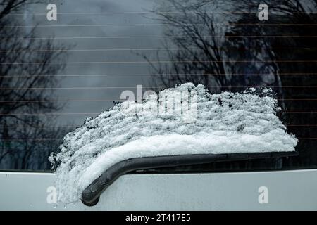 Scheibenwischer der Heckscheibe eines Autos, der mit einer Schneeschicht bedeckt ist, die infolge der Erwärmung mit Heizleisten von der Scheibe aufgetaut wurde, Nahaufnahme. Stockfoto