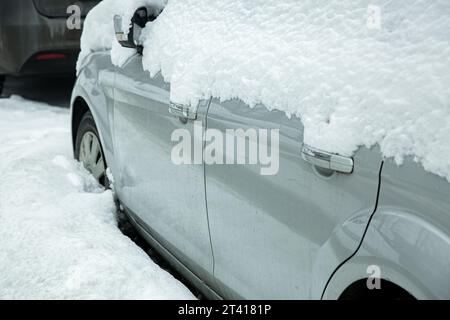 Fahrzeugseite mit eingeklapptem Rückspiegel mit Blinker und Fahrzeugtüren mit verchromten Griffen, die an einem verschneiten Wintertag mit Schnee bedeckt sind Stockfoto
