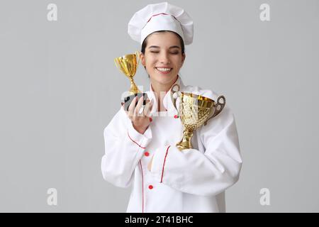 Weibliche Köchin mit goldenen Tassen auf hellem Hintergrund Stockfoto